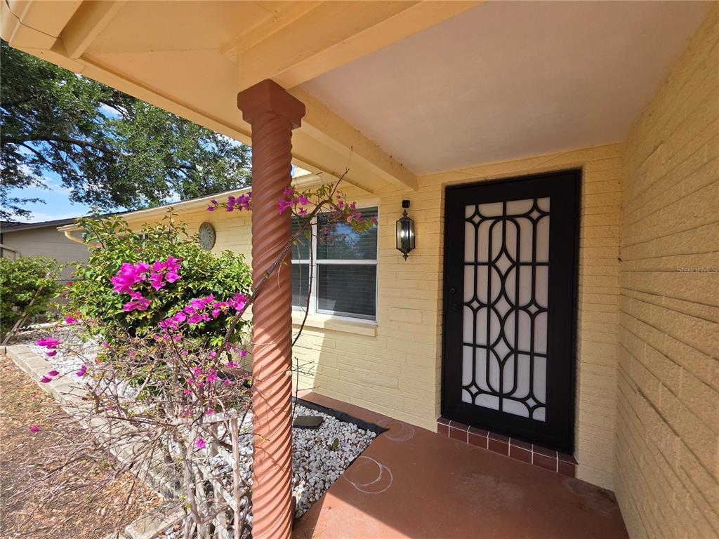 A yellow brick house exterior features a covered porch, a spiral column, and a decorative door — 4832 ELMWOOD STREET, NEW PORT RICHEY, FL