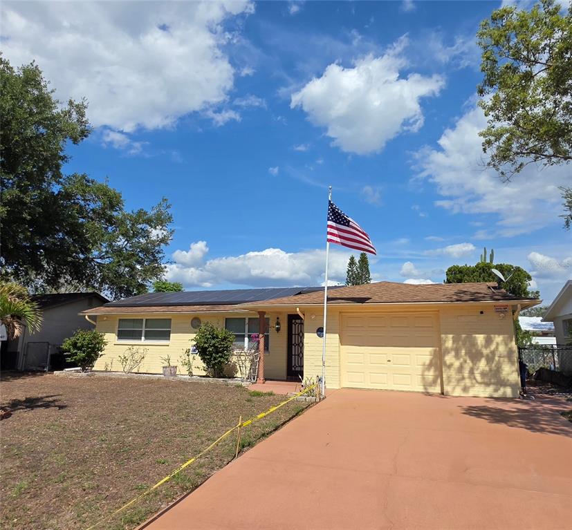 A single-story yellow house with a garage, solar panels, and an American flag in front — 4832 ELMWOOD STREET, NEW PORT RICHEY, FL
