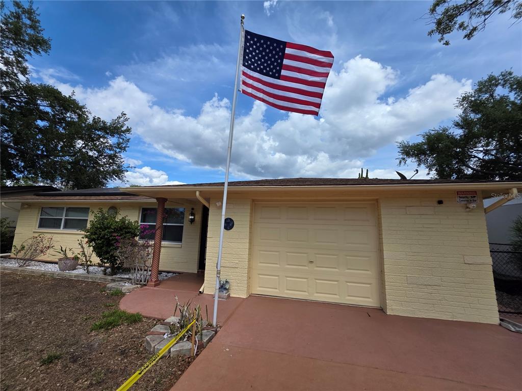 A single-story house with yellow brick siding, a garage, and an American flag out front — 4832 ELMWOOD STREET, NEW PORT RICHEY, FL
