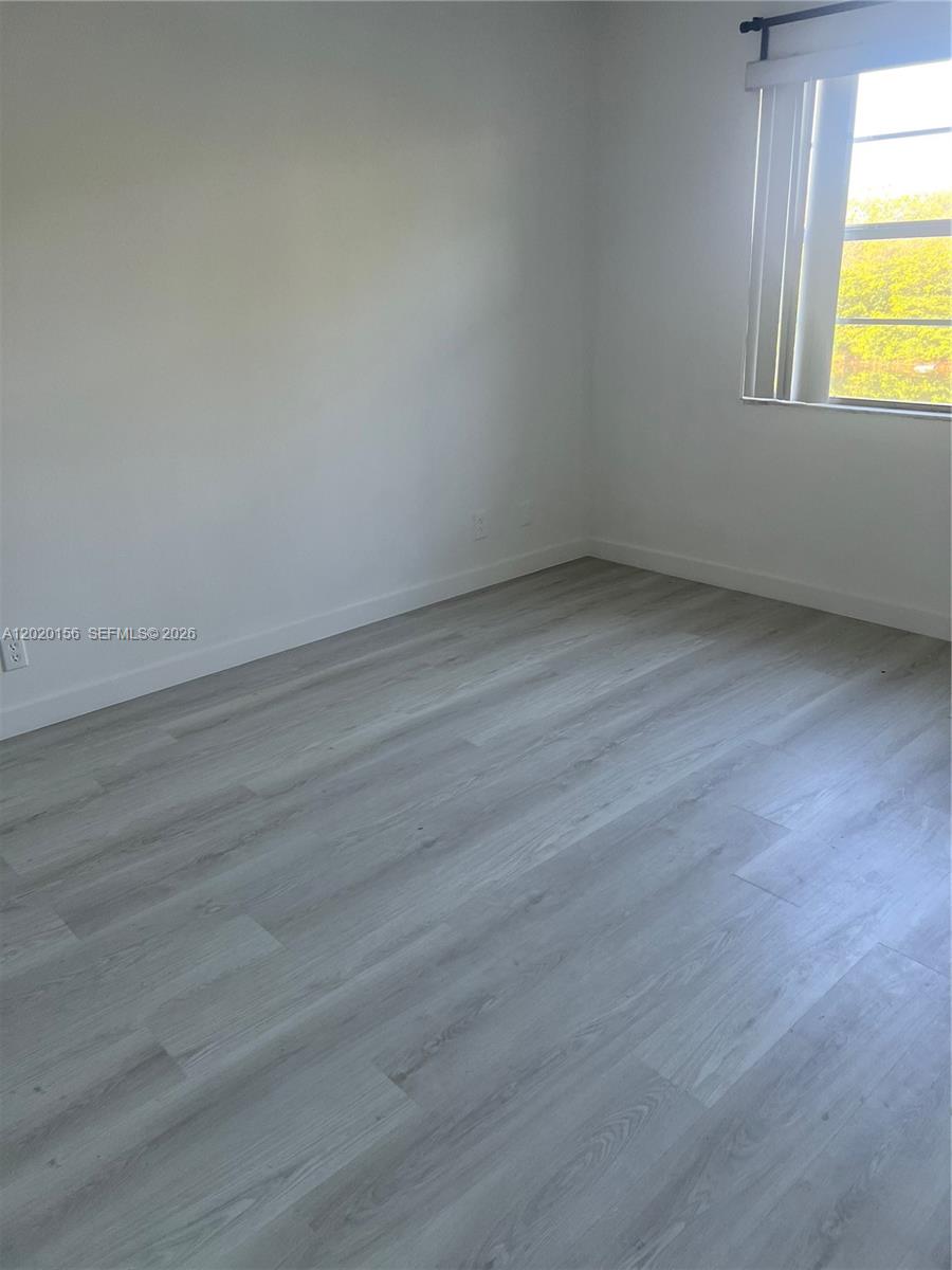 An empty bedroom features white walls, light-colored wood-look flooring, and a window with blinds — 3621 NW 95th Ter # 523, Sunrise FL 33351, SUNRISE, FL