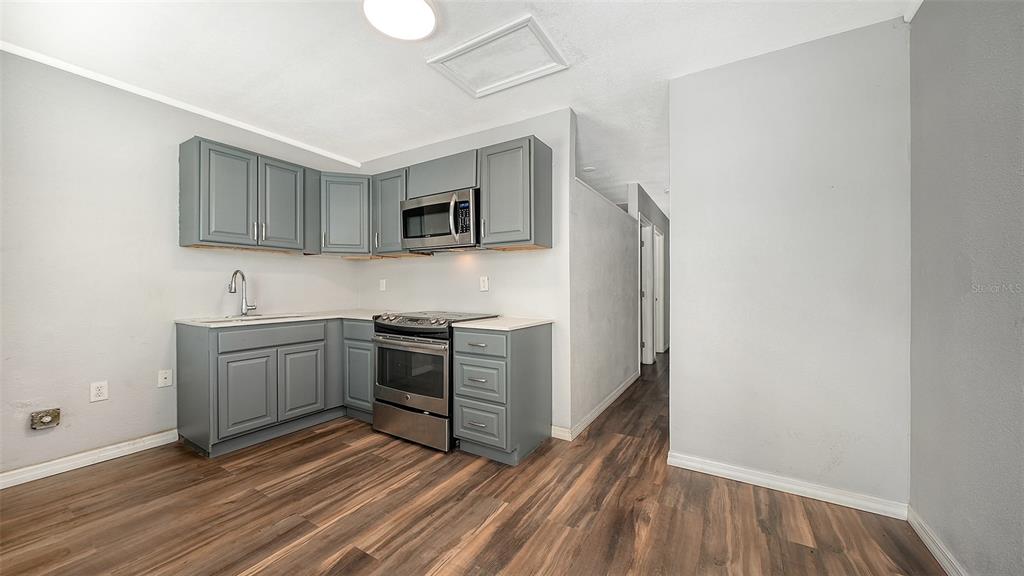 A kitchen features gray cabinets, stainless steel appliances, and wood-look flooring — 1004 27TH AVENUE W, BRADENTON, FL