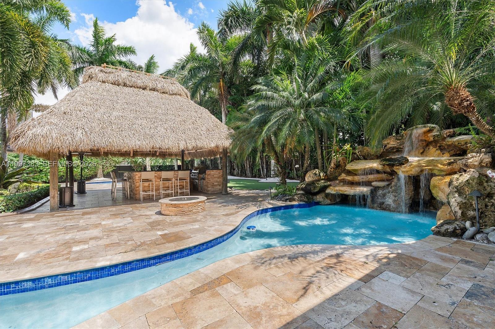 A backyard features a thatched-roof tiki bar, a stone waterfall, and a swimming pool — 14800 SW 166th St, Miami FL 33187, MIAMI, FL