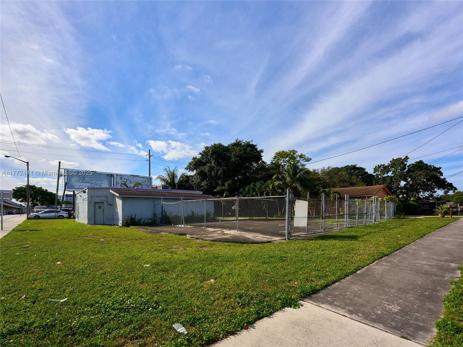 A fenced-in paved lot sits next to a small, light-colored building under a blue sky — 5832 NW 27th Ave, Miami FL 33142, MIAMI, FL