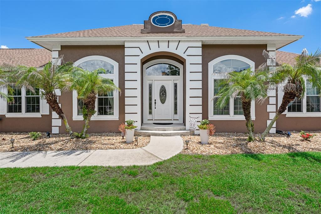 A brown stucco house with white trim, arched windows, and palm trees in the front yard — 8627 BOW COURT, ORLANDO, FL