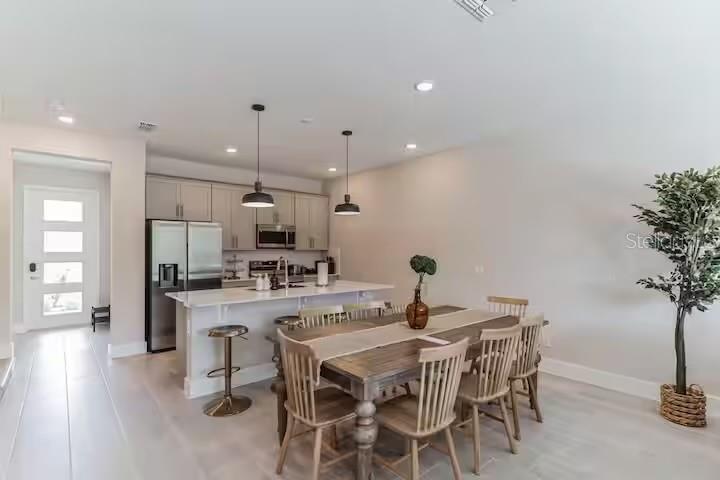 A modern kitchen with light cabinetry and a dining area featuring a wooden table — 7842 SPECTRUM DRIVE, REUNION, FL