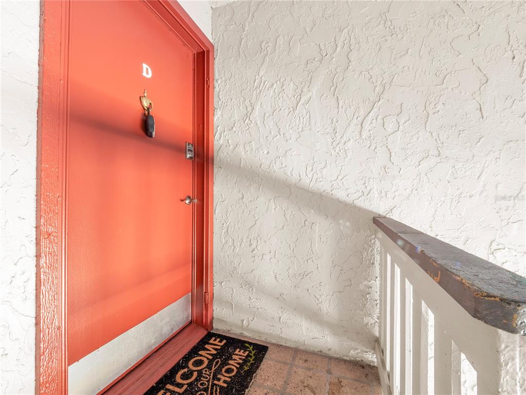 An orange front door labeled D is situated on a textured exterior landing — 4036 CORTEZ DRIVE UNIT D, TAMPA, FL