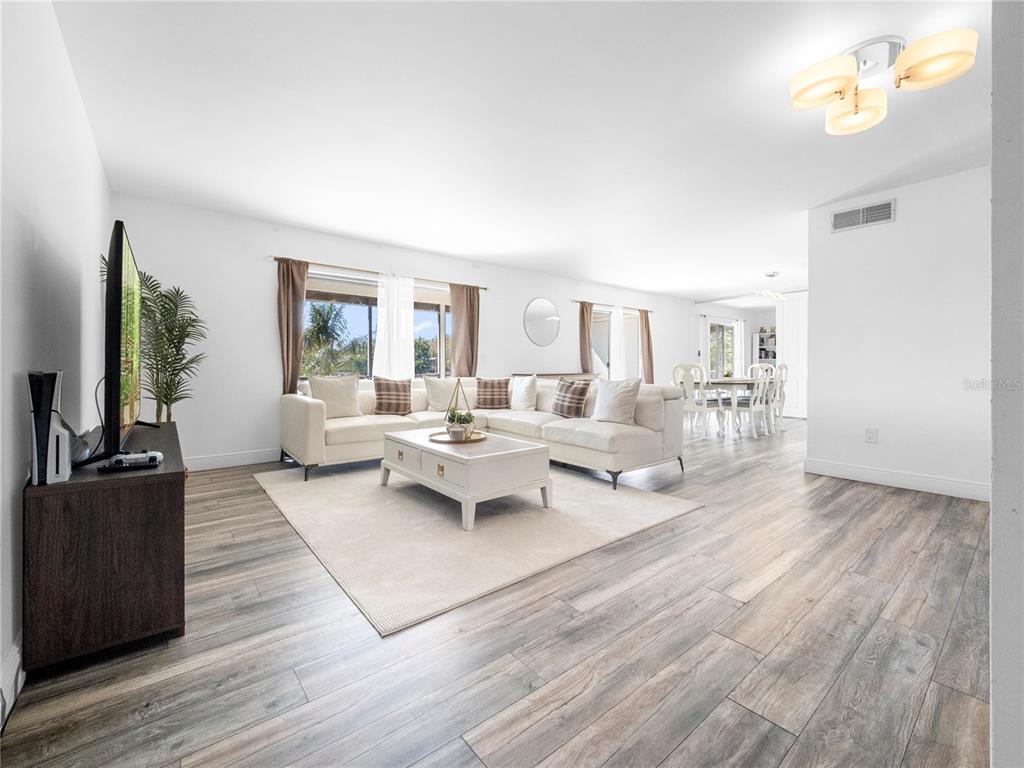 A living room with white walls, wood-look flooring, a sectional sofa, and a dining area — 4036 CORTEZ DRIVE UNIT D, TAMPA, FL