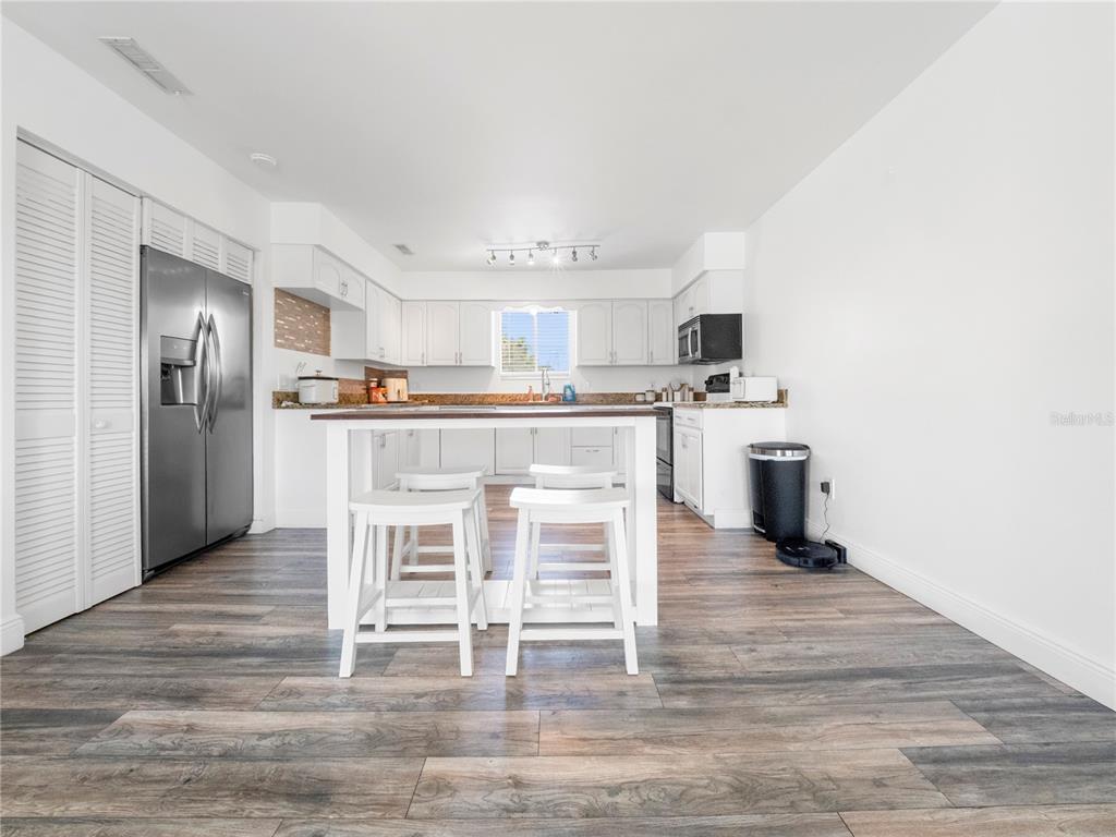 A kitchen features white cabinetry, stainless steel appliances, a center island, and wood-look flooring — 4036 CORTEZ DRIVE UNIT D, TAMPA, FL