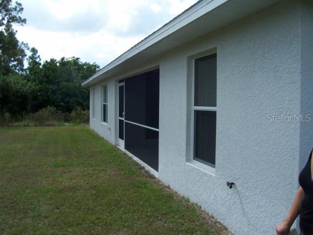 The exterior side of a white stucco house features a screened-in porch and windows — 1491 GLENVIEW ROAD, NORTH PORT, FL