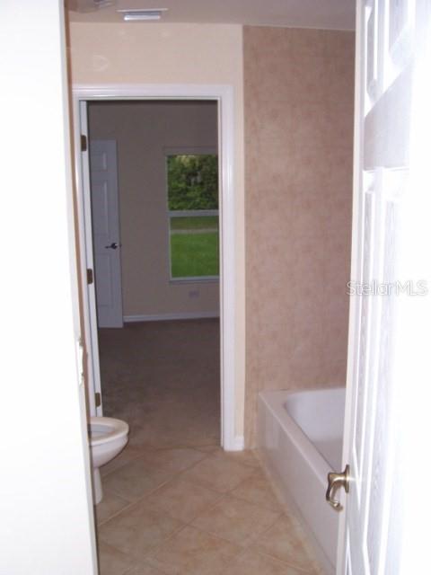 A bathroom with a white tub and toilet, leading into a bedroom with a window — 1491 GLENVIEW ROAD, NORTH PORT, FL