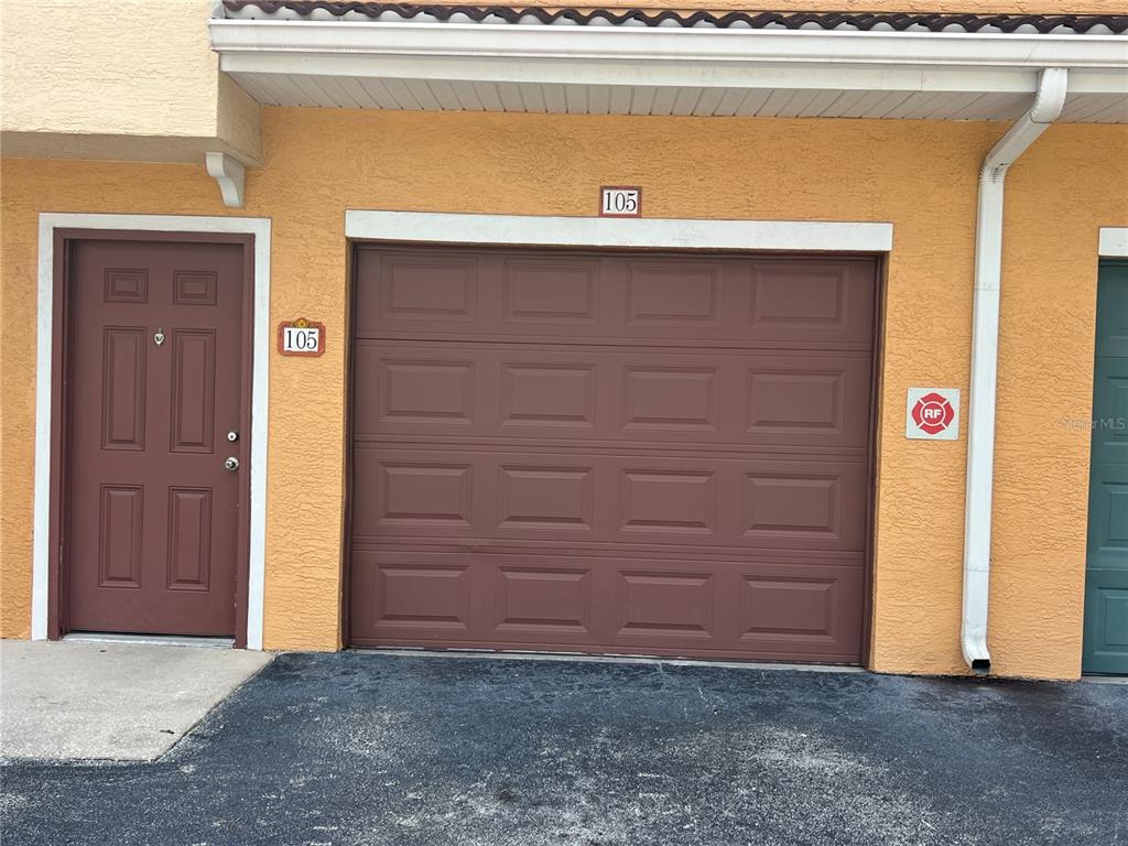 An exterior view of a residential garage door and adjacent entry door labeled 105 — 12414 BALERIA COVE UNIT 105, ORLANDO, FL