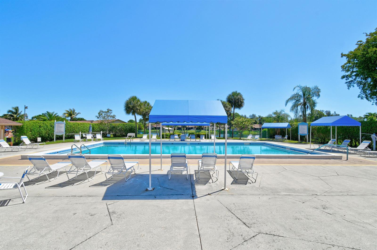 A rectangular outdoor swimming pool features blue shade canopies and lounge chairs on a concrete deck — 4 Knightsbridge Lane, Boynton Beach FL 33426, BOYNTON BEACH, FL