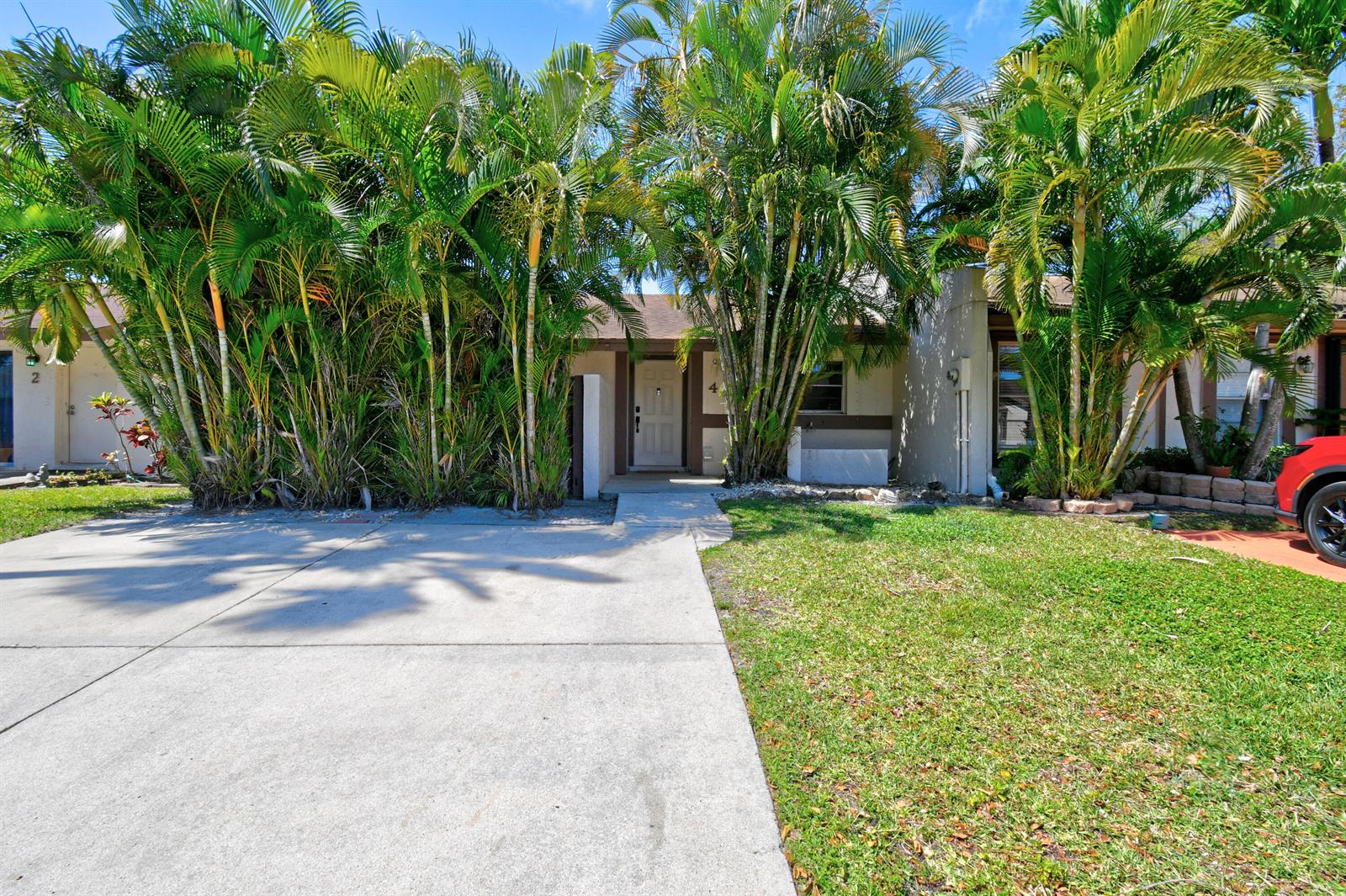A concrete driveway leads to the front entrance of a house surrounded by palm trees — 4 Knightsbridge Lane, Boynton Beach FL 33426, BOYNTON BEACH, FL