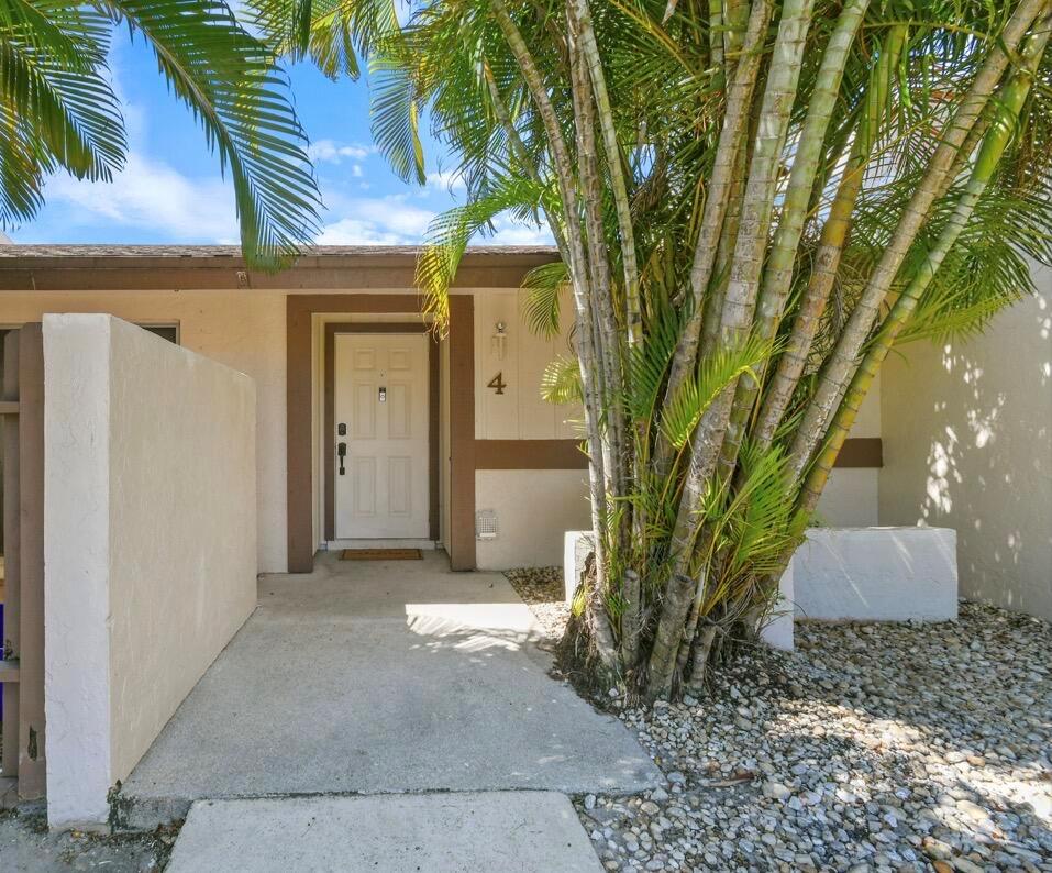 The exterior of a residential unit features a white front door, palm trees, and gravel — 4 Knightsbridge Lane, Boynton Beach FL 33426, BOYNTON BEACH, FL