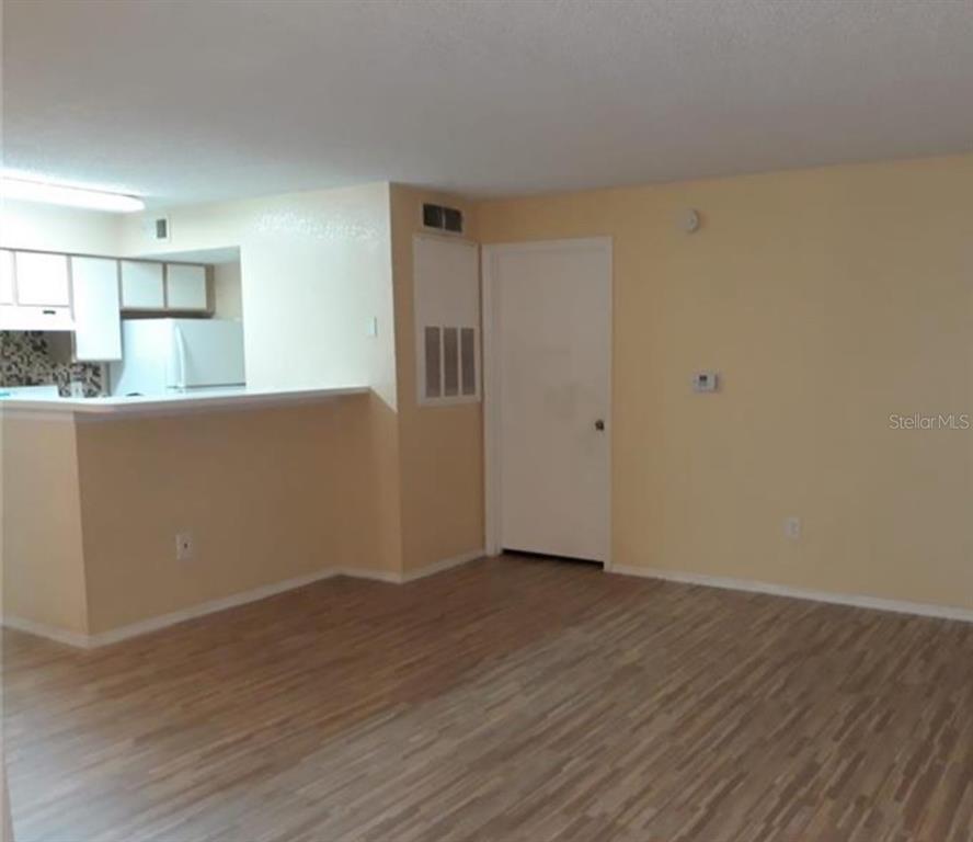 A living area with light-colored walls and wood-look flooring opens to a kitchen counter — 2217 GRAND CAYMAN COURT UNIT 1218, KISSIMMEE, FL