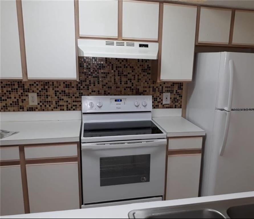 A kitchen features white cabinets, a white stove, a white refrigerator, and a mosaic backsplash — 2217 GRAND CAYMAN COURT UNIT 1218, KISSIMMEE, FL