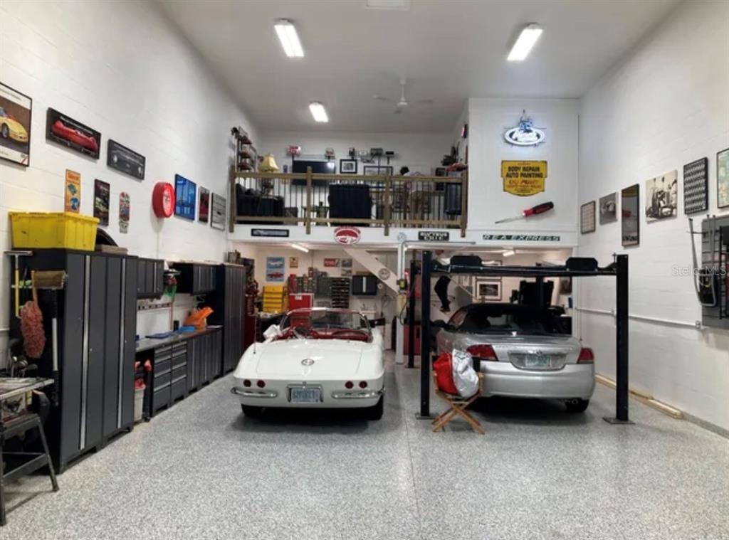 A spacious garage features a white convertible, a car lift, storage cabinets, and a loft area — 144 ANCHOR ROAD UNIT B-5, ROTONDA WEST, FL