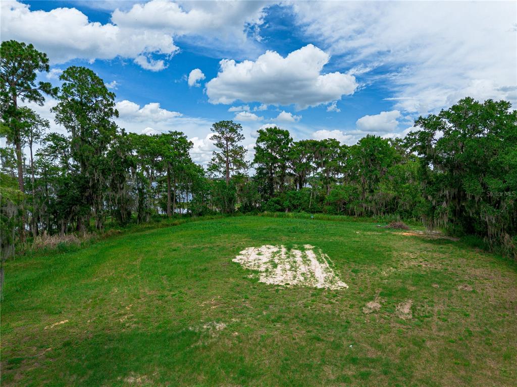 A grassy, cleared lot features a patch of exposed sand with trees bordering a lake — MANTOVA COURT, ORLANDO, FL