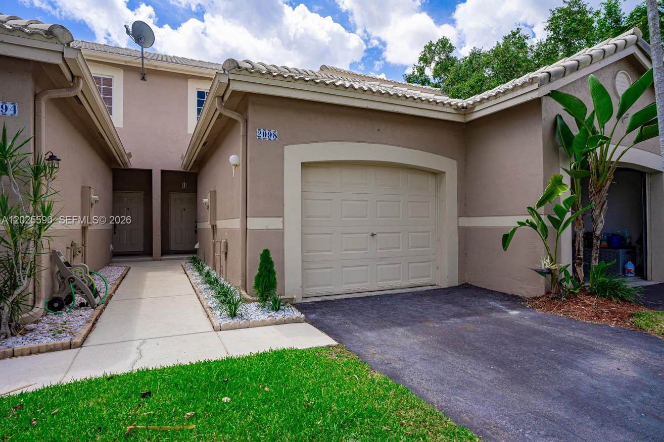 A tan townhouse exterior features a single-car garage, a concrete walkway, and a small lawn — 2098 Madeira Dr, Weston FL 33327, WESTON, FL