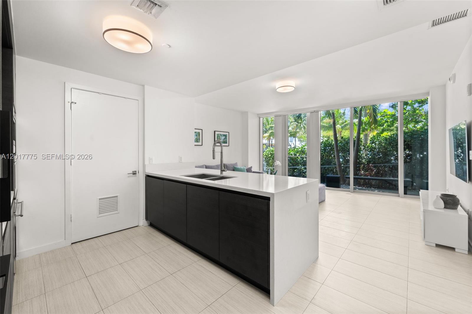 A modern kitchen features a dark island with a white countertop and large glass windows — 1 Collins Ave # 108, Miami Beach FL 33139, MIAMI BEACH, FL