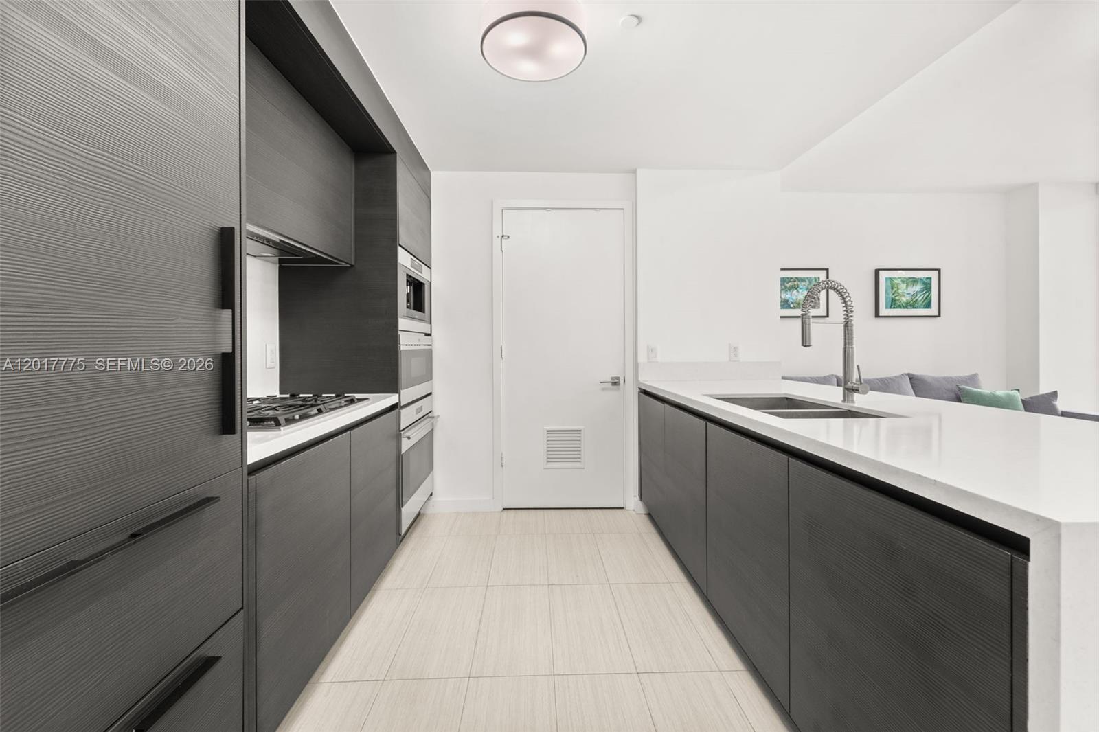 A modern kitchen features dark wood cabinetry, white countertops, stainless steel appliances, and tile flooring — 1 Collins Ave # 108, Miami Beach FL 33139, MIAMI BEACH, FL