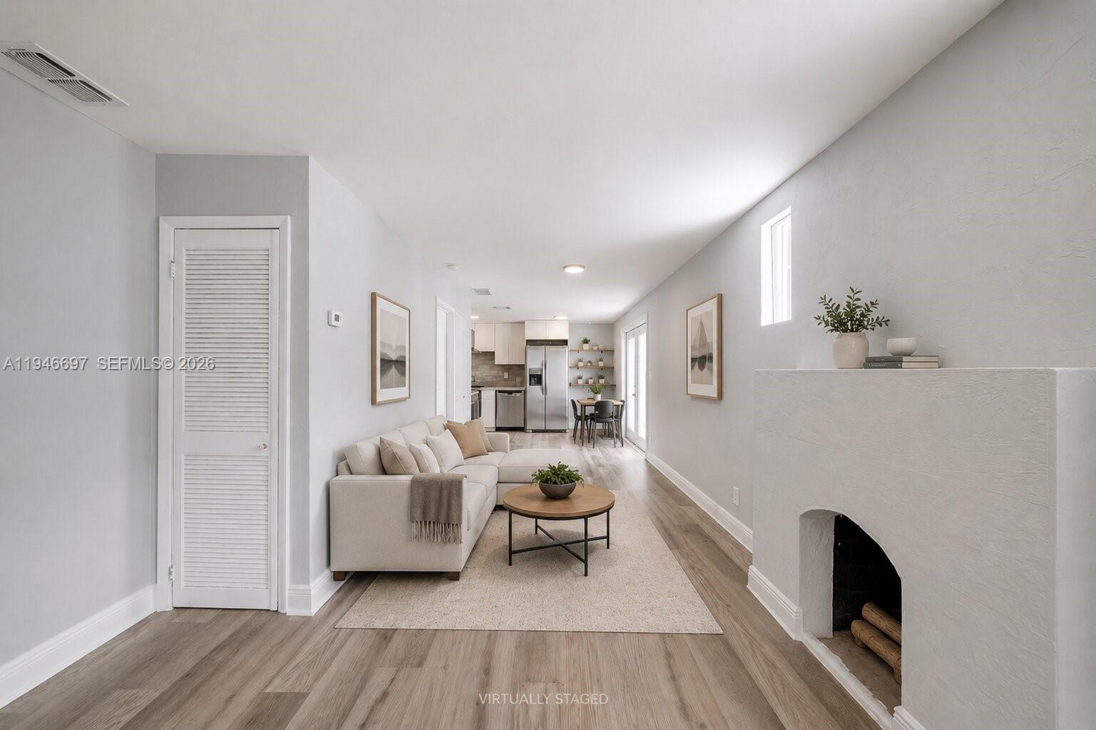 A living room with a fireplace, sofa, and open-concept kitchen features light wood-look flooring — 1726 Roosevelt St, Hollywood FL 33020, HOLLYWOOD, FL