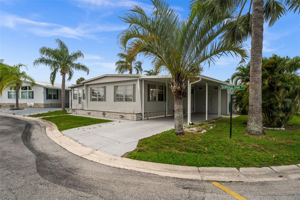 A light-colored manufactured home features a carport, palm trees, and a street sign — 3318 SHINGLE OAK TERRACE, SARASOTA, FL