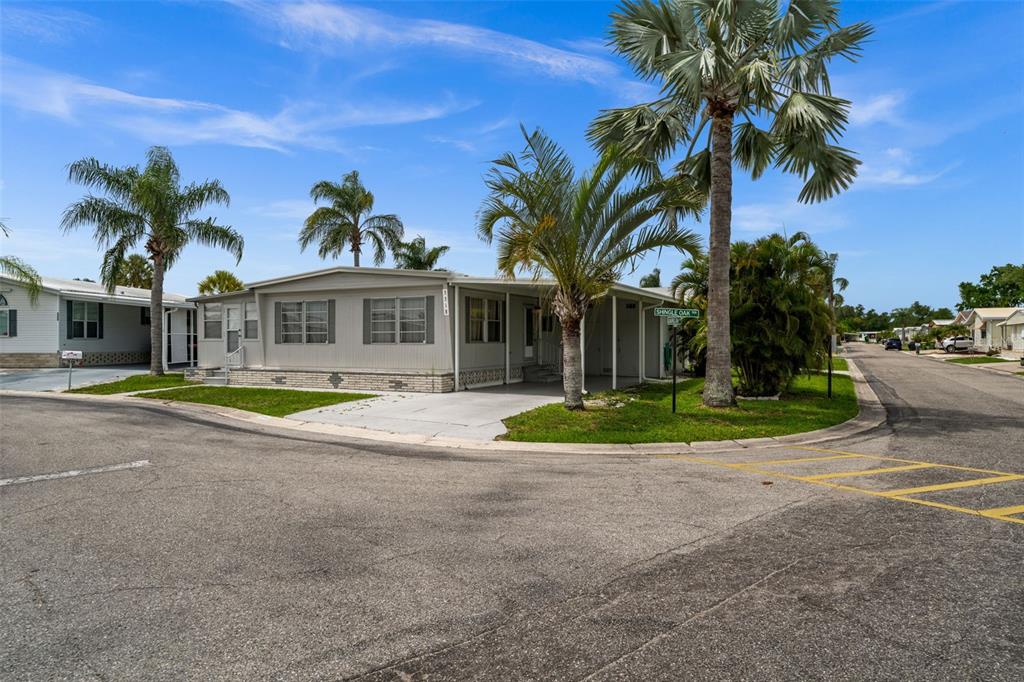 A single-story manufactured home with a carport sits on a corner lot with palm trees — 3318 SHINGLE OAK TERRACE, SARASOTA, FL