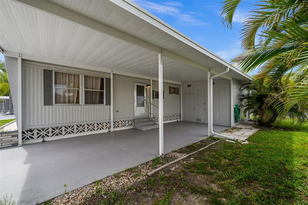 A mobile home exterior features a covered carport, concrete patio, and white vertical siding — 3318 SHINGLE OAK TERRACE, SARASOTA, FL