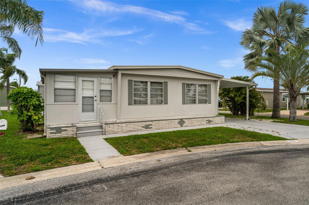 A single-story manufactured home with light siding, a brick base, and a carport — 3318 SHINGLE OAK TERRACE, SARASOTA, FL