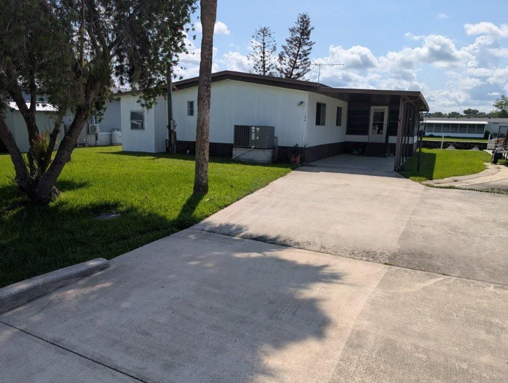A single-story mobile home with a concrete driveway, carport, and a grassy front yard — 154 MOONLITE DRIVE, WELAKA, FL