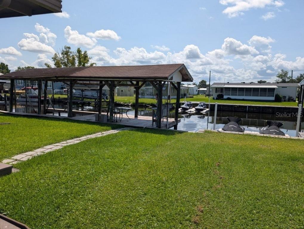 A grassy yard leads to a wooden boat dock with a covered slip on a canal — 154 MOONLITE DRIVE, WELAKA, FL