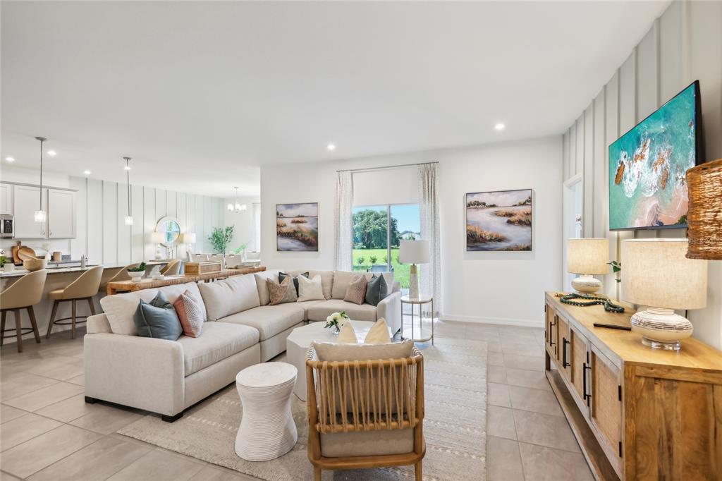 A bright, open-concept living room features a large sectional sofa, wooden console, and tile flooring — 12906 CARA COURT, GRAND ISLAND, FL