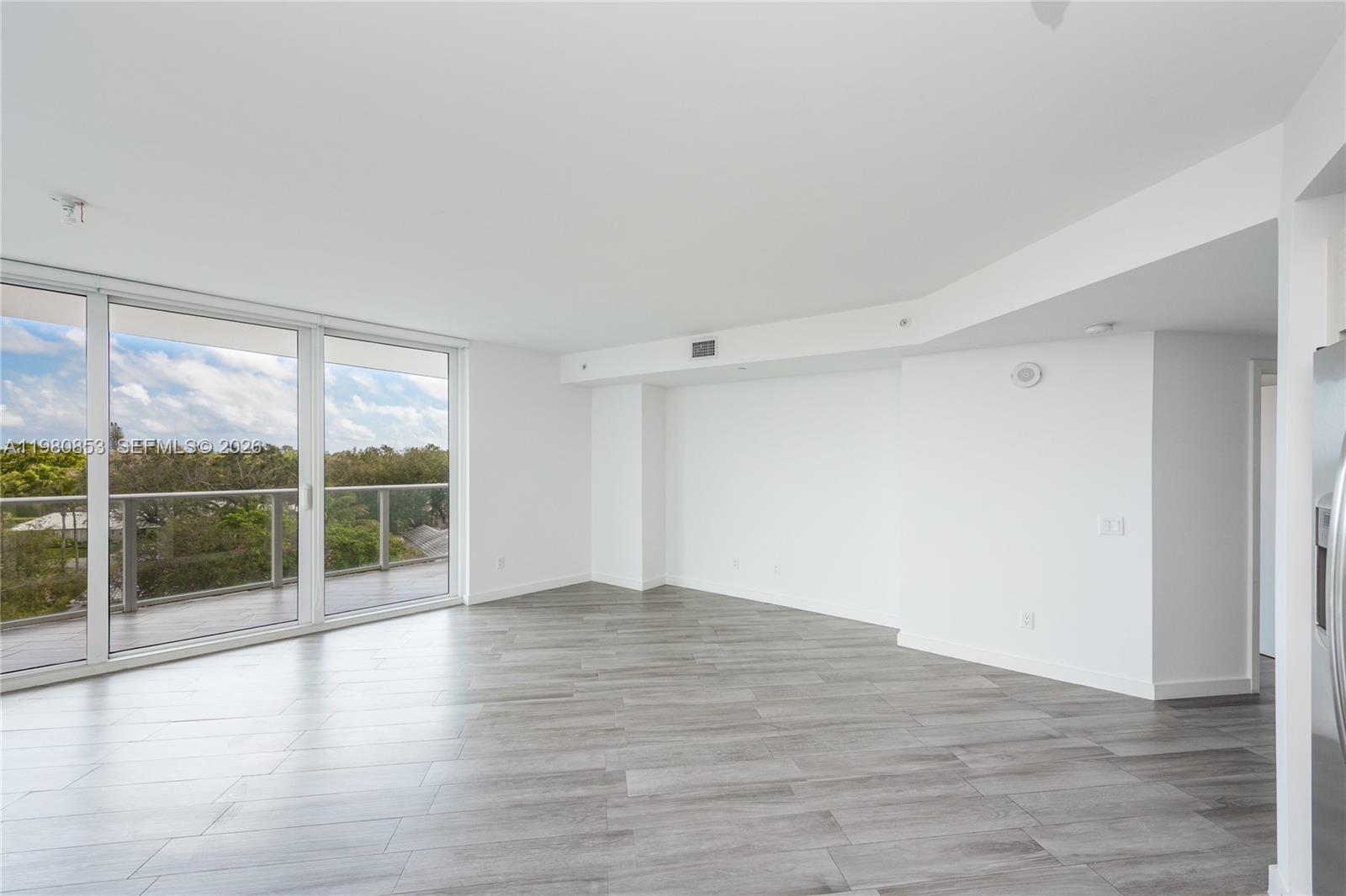 An empty room with gray wood-look tile flooring, white walls, and a glass balcony door — 4250 Biscayne Blvd # 502, Miami FL 33137, MIAMI, FL