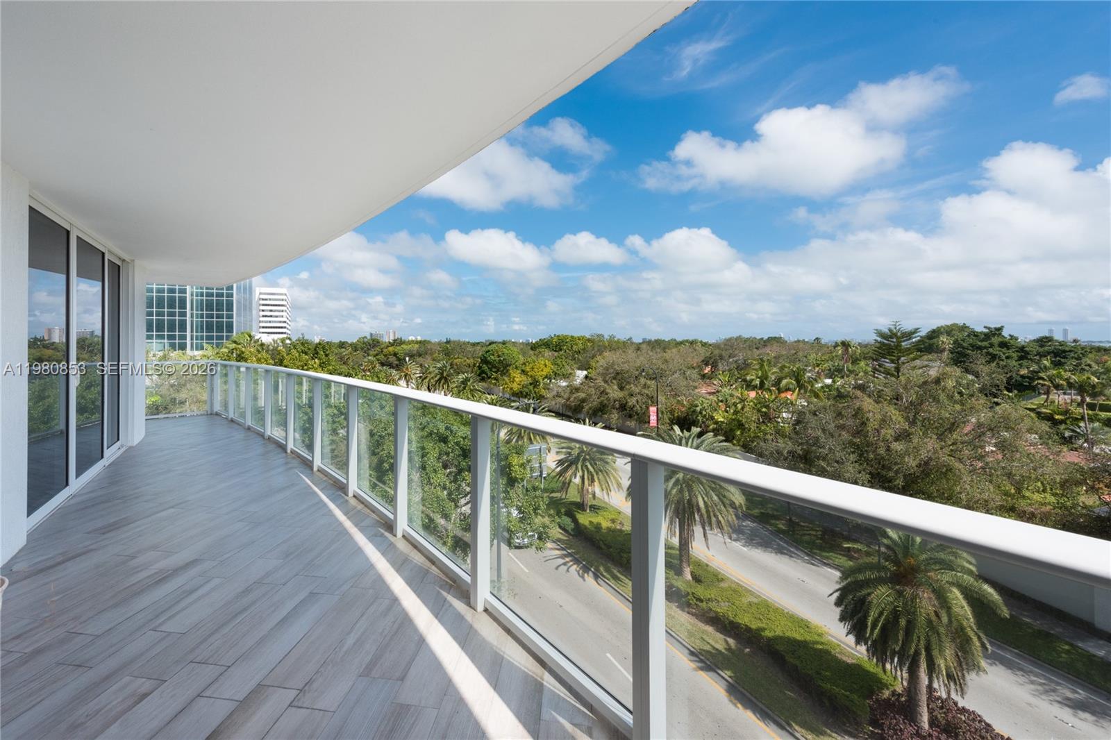 A balcony with glass railings overlooks a road surrounded by trees and distant buildings — 4250 Biscayne Blvd # 502, Miami FL 33137, MIAMI, FL