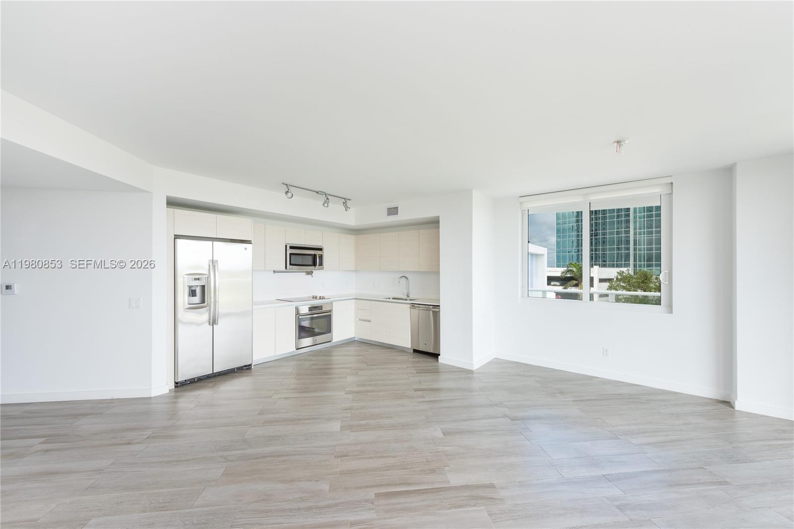 A modern kitchen with white cabinets and stainless steel appliances opens into a living area — 4250 Biscayne Blvd # 502, Miami FL 33137, MIAMI, FL