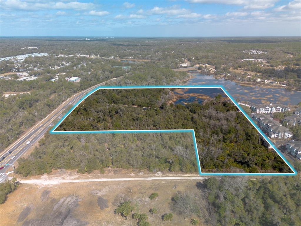 An aerial view shows a large, L-shaped wooded lot outlined in blue next to a road — VETERANS MEMORIAL PARKWAY, ORANGE CITY, FL