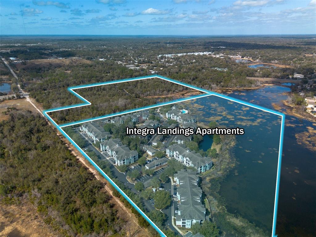 An aerial view shows an apartment complex surrounded by wooded areas and a large pond — VETERANS MEMORIAL PARKWAY, ORANGE CITY, FL