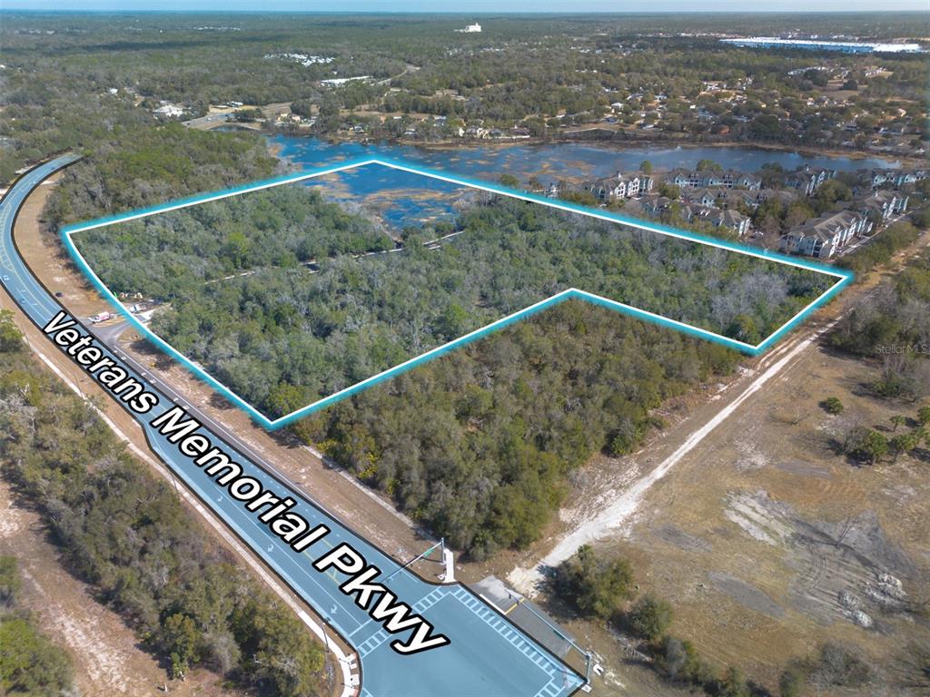 An aerial view shows a wooded, undeveloped plot of land outlined in blue near a highway — VETERANS MEMORIAL PARKWAY, ORANGE CITY, FL