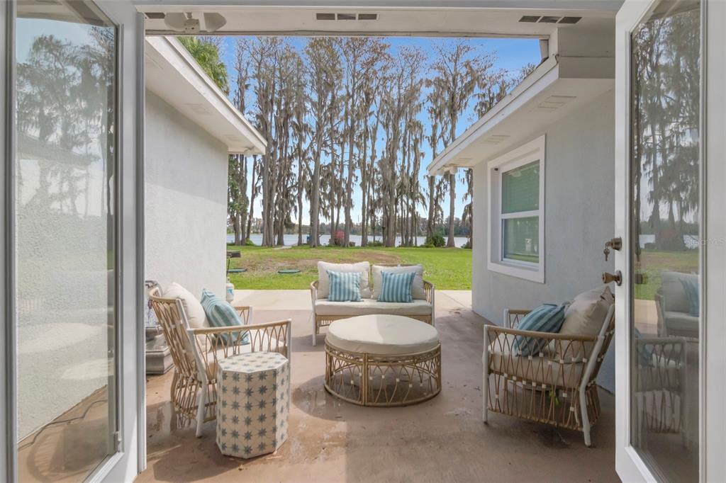 A covered patio features outdoor furniture overlooking a grassy yard and a lake with trees — 19207 CROOKED LANE, LUTZ, FL