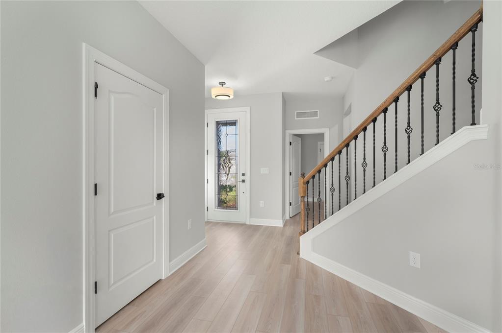 A bright entryway features light wood flooring, a staircase with iron railings, and a front door — 7895 SOMERSWORTH DRIVE, KISSIMMEE, FL