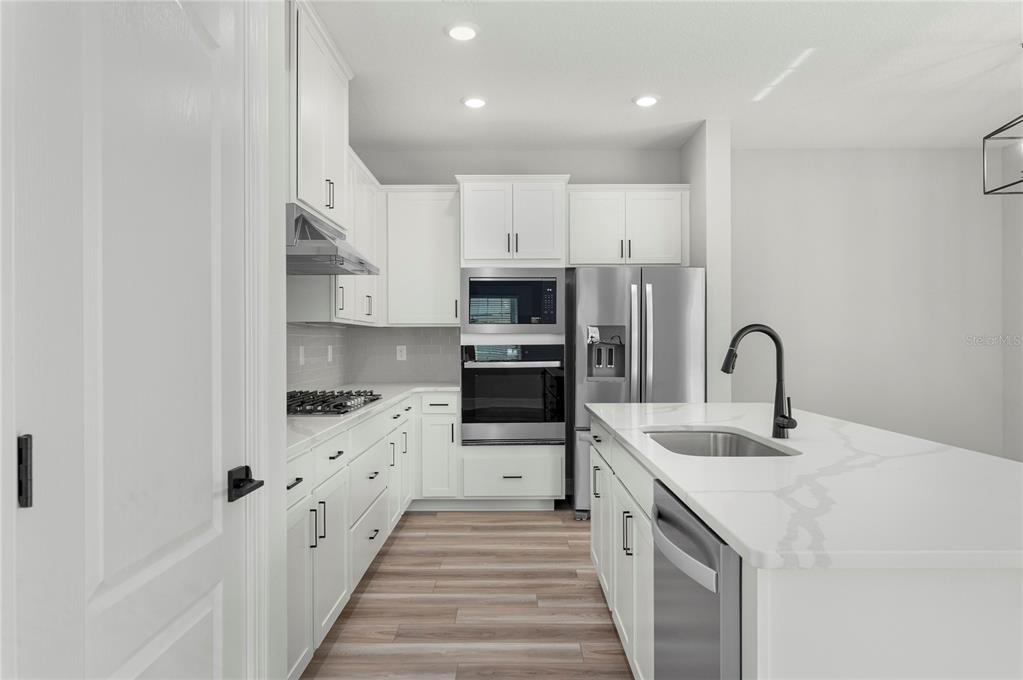 A modern kitchen features white cabinetry, stainless steel appliances, and a white quartz island — 7895 SOMERSWORTH DRIVE, KISSIMMEE, FL