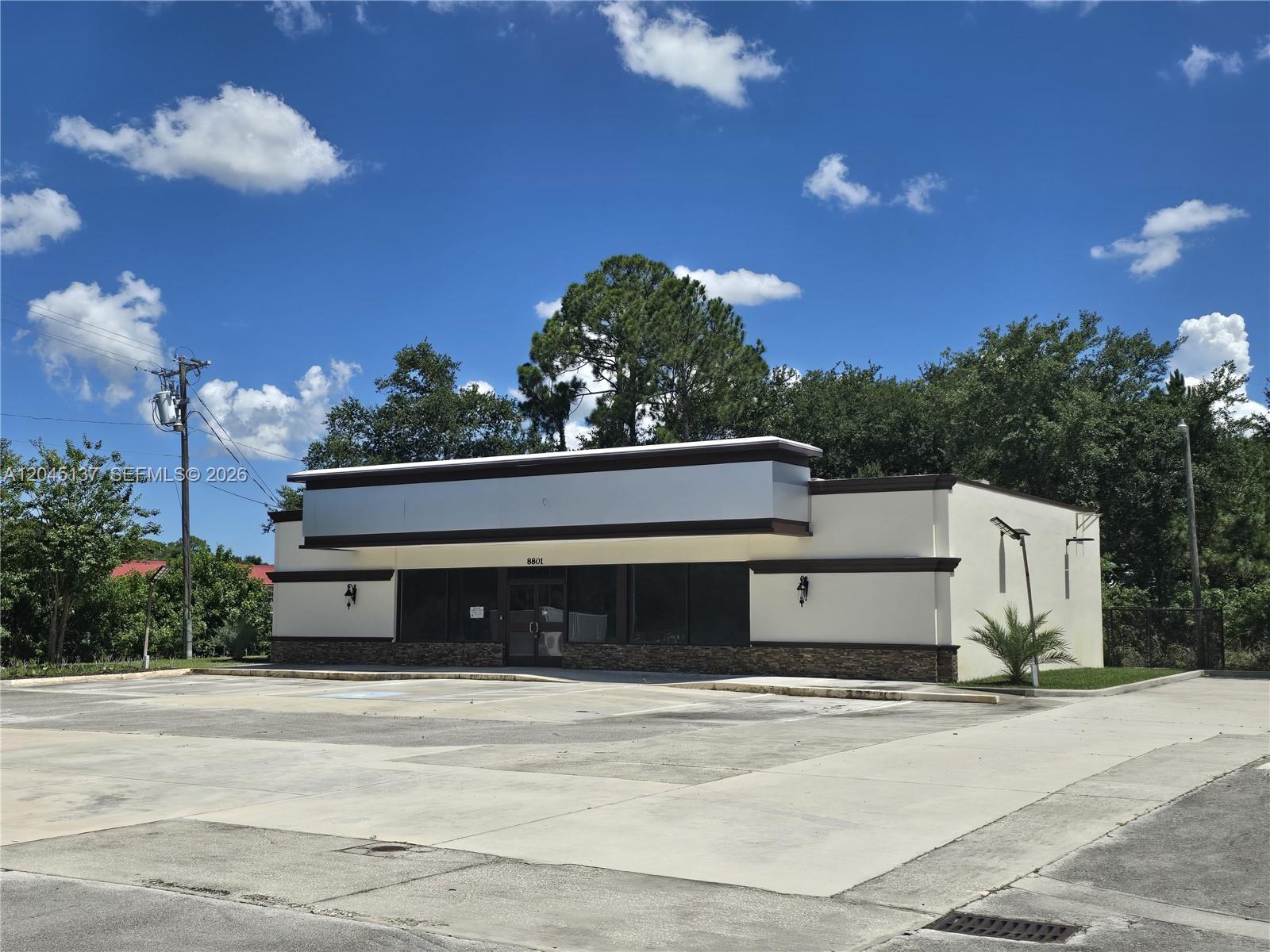A single-story commercial building with a large parking lot under a blue sky — 8801 20th St, Vero Beach FL 32966, VERO BEACH, FL