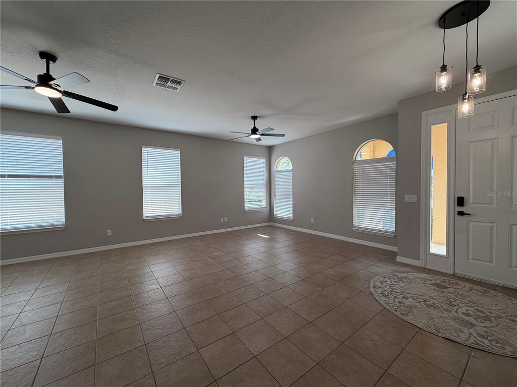 An empty room features tile flooring, ceiling fans, multiple windows with blinds, and a doorway — 528 ORANGE COSMOS BOULEVARD, DAVENPORT, FL