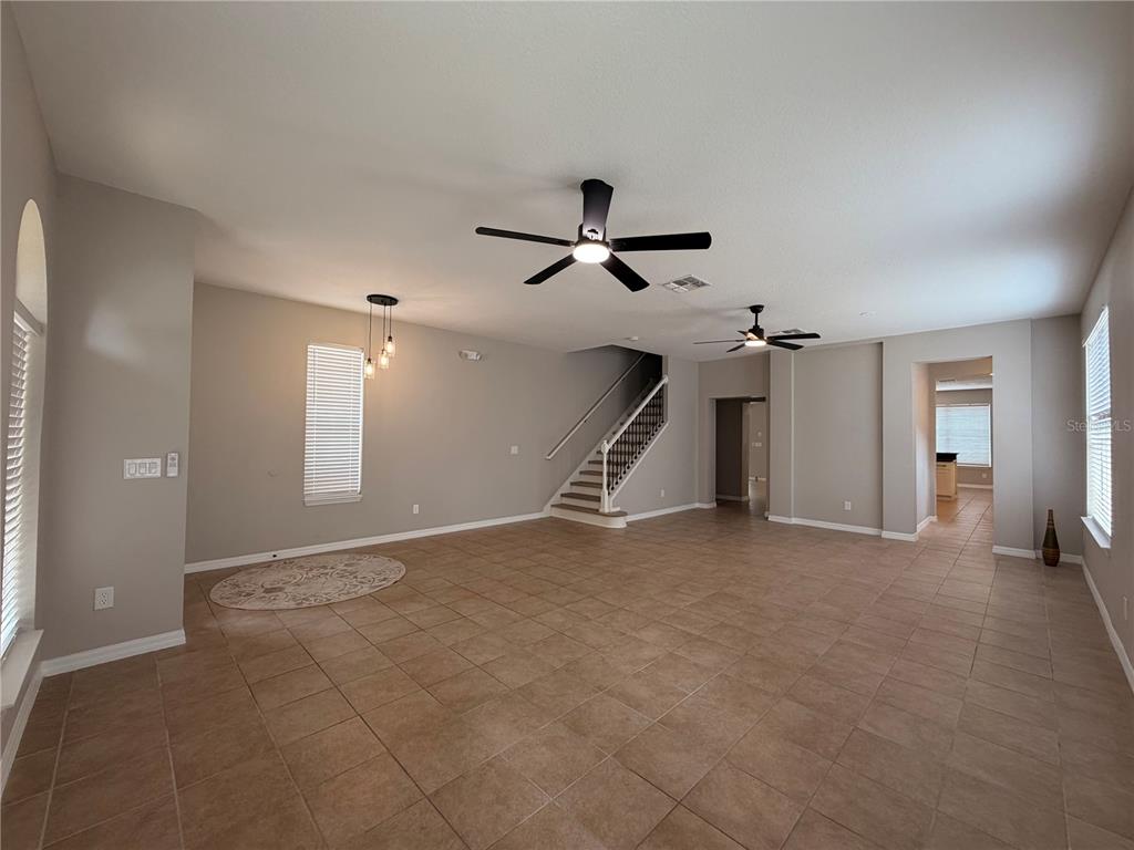 An open-concept living area features tile flooring, two ceiling fans, and a staircase — 528 ORANGE COSMOS BOULEVARD, DAVENPORT, FL