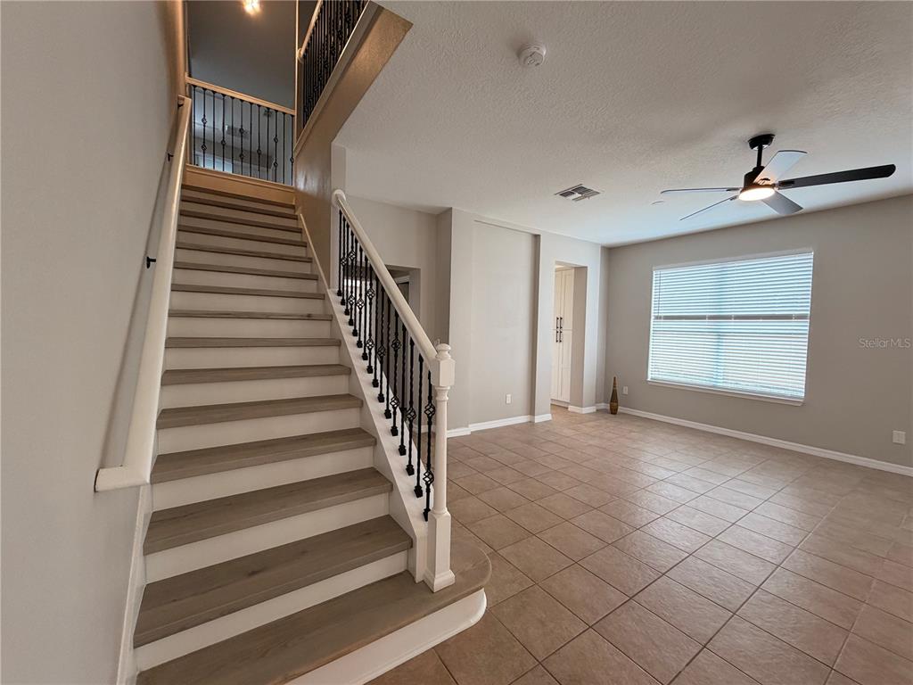 A staircase with wood-look treads and black metal railings sits beside a tiled living area — 528 ORANGE COSMOS BOULEVARD, DAVENPORT, FL