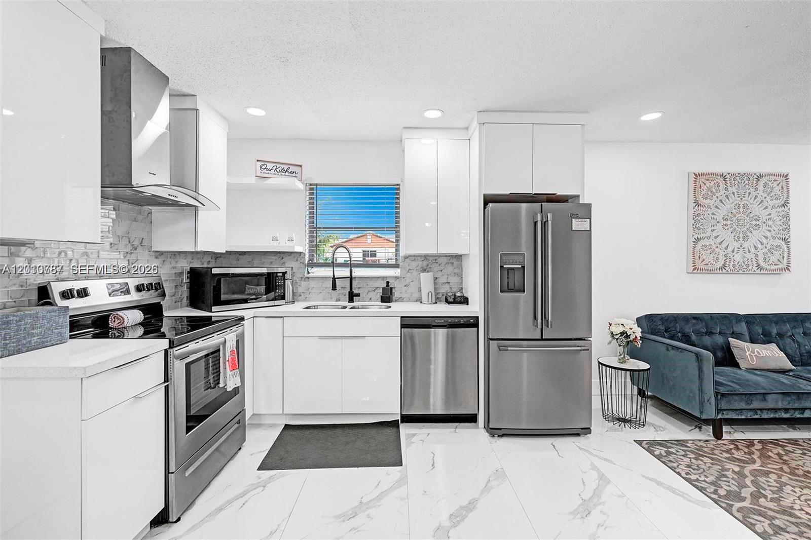 A modern kitchen features white cabinets, stainless steel appliances, and marble-look tile flooring — 2338 Fillmore St # 2A, Hollywood FL 33020, HOLLYWOOD, FL