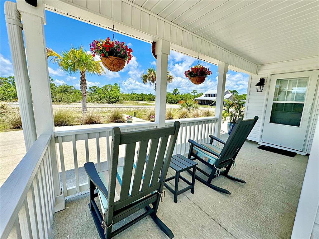 A covered front porch features two rocking chairs, a small table, and hanging flower baskets — 260 BLUE HERON DRIVE, EASTPOINT, FL