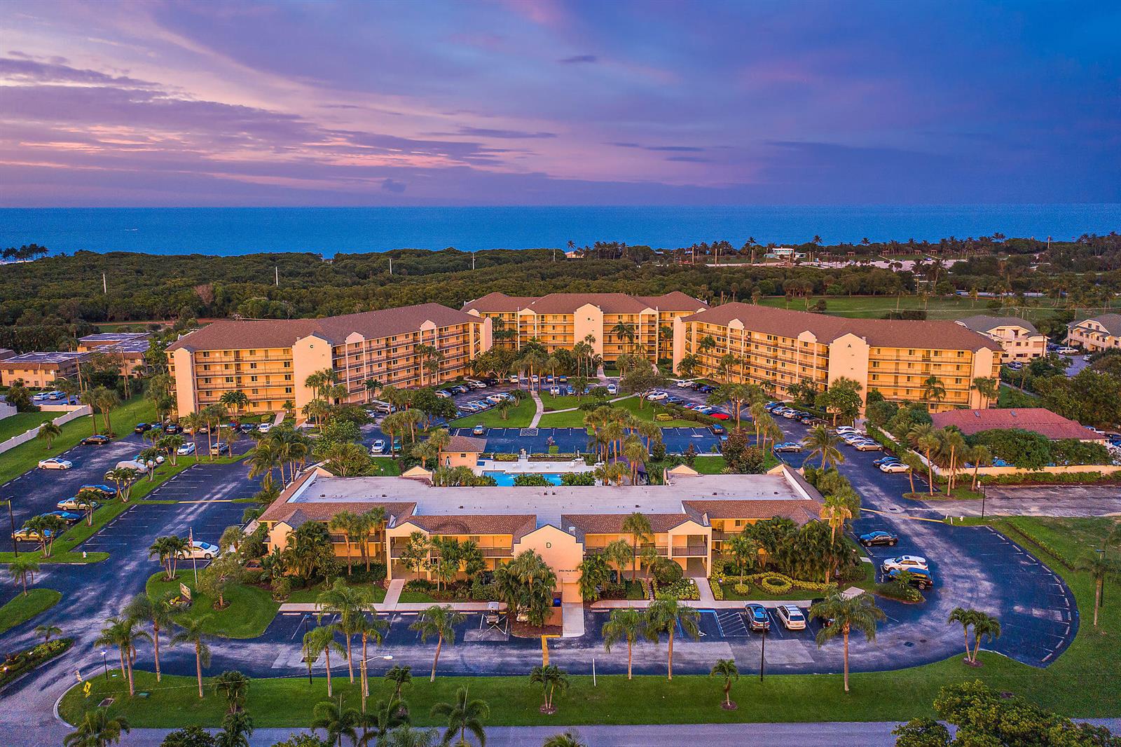 An aerial view of a multi-story apartment complex with a central pool and parking lots — 275 Palm Avenue # C402, Jupiter FL 33477, JUPITER, FL