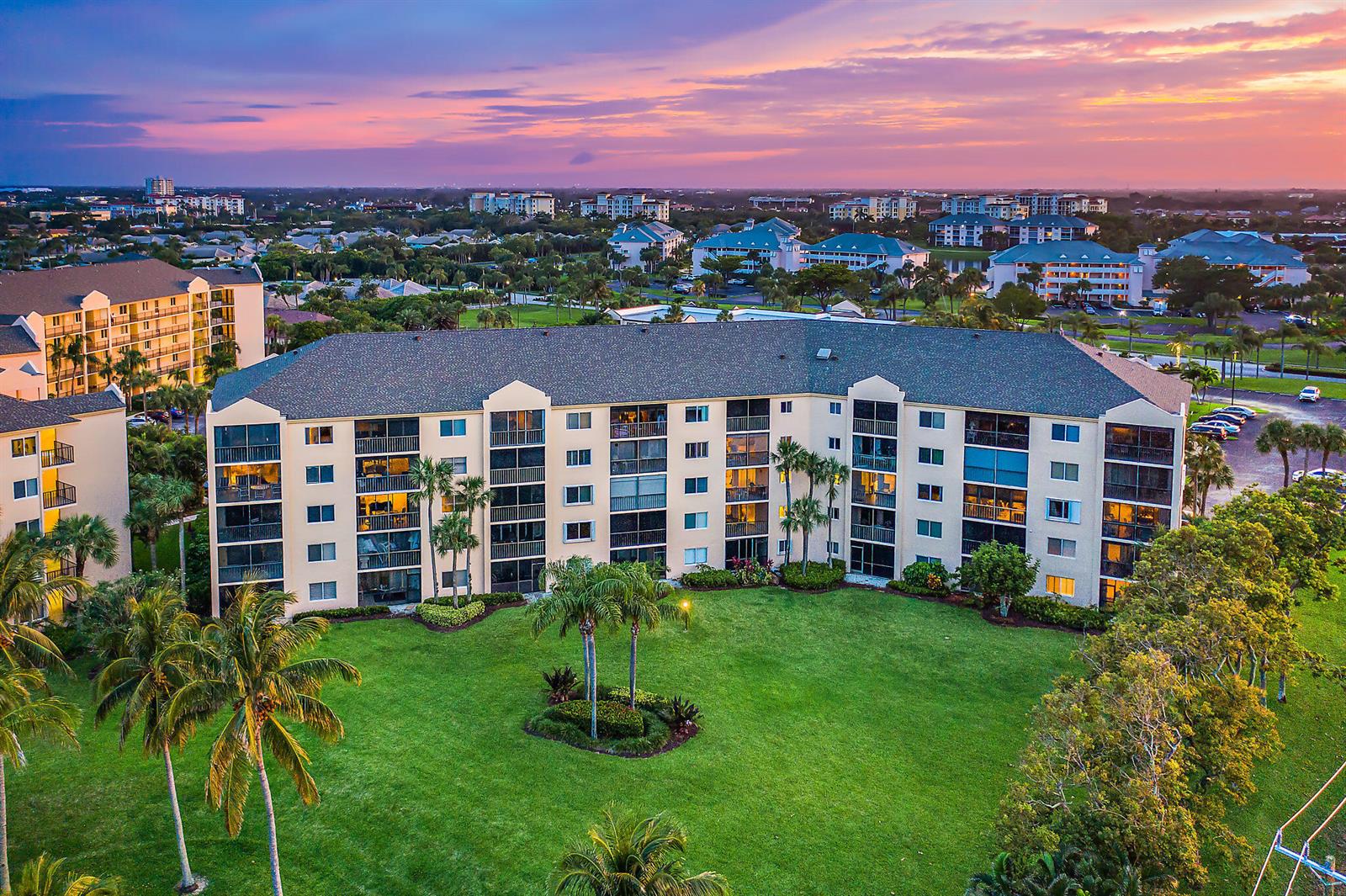 An aerial view of a multi-story apartment building surrounded by a lawn and palm trees — 275 Palm Avenue # C402, Jupiter FL 33477, JUPITER, FL